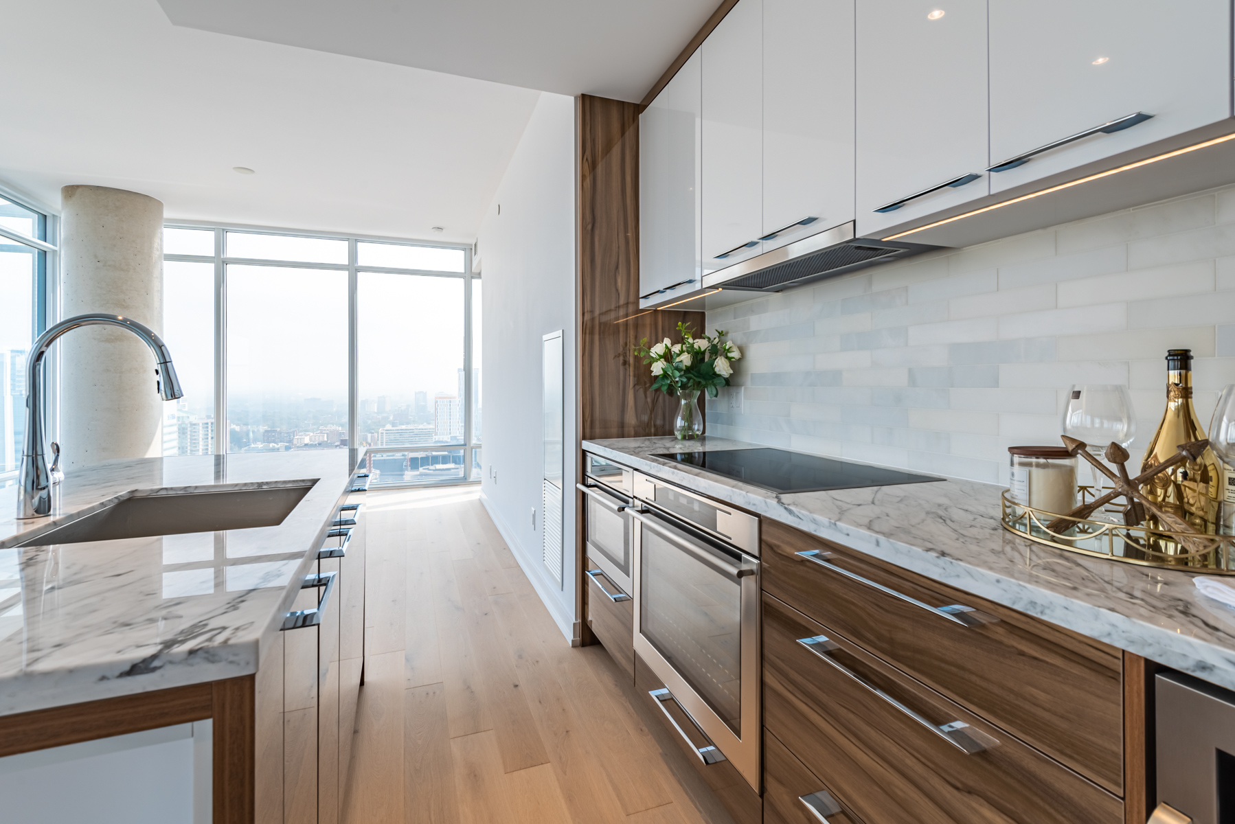 Condo kitchen with white marble counters, shiny cabinets and a tiled back-splash.