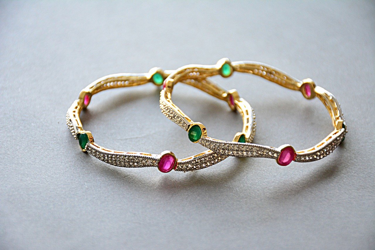 Pair of gold bracelets with pink and green gems.