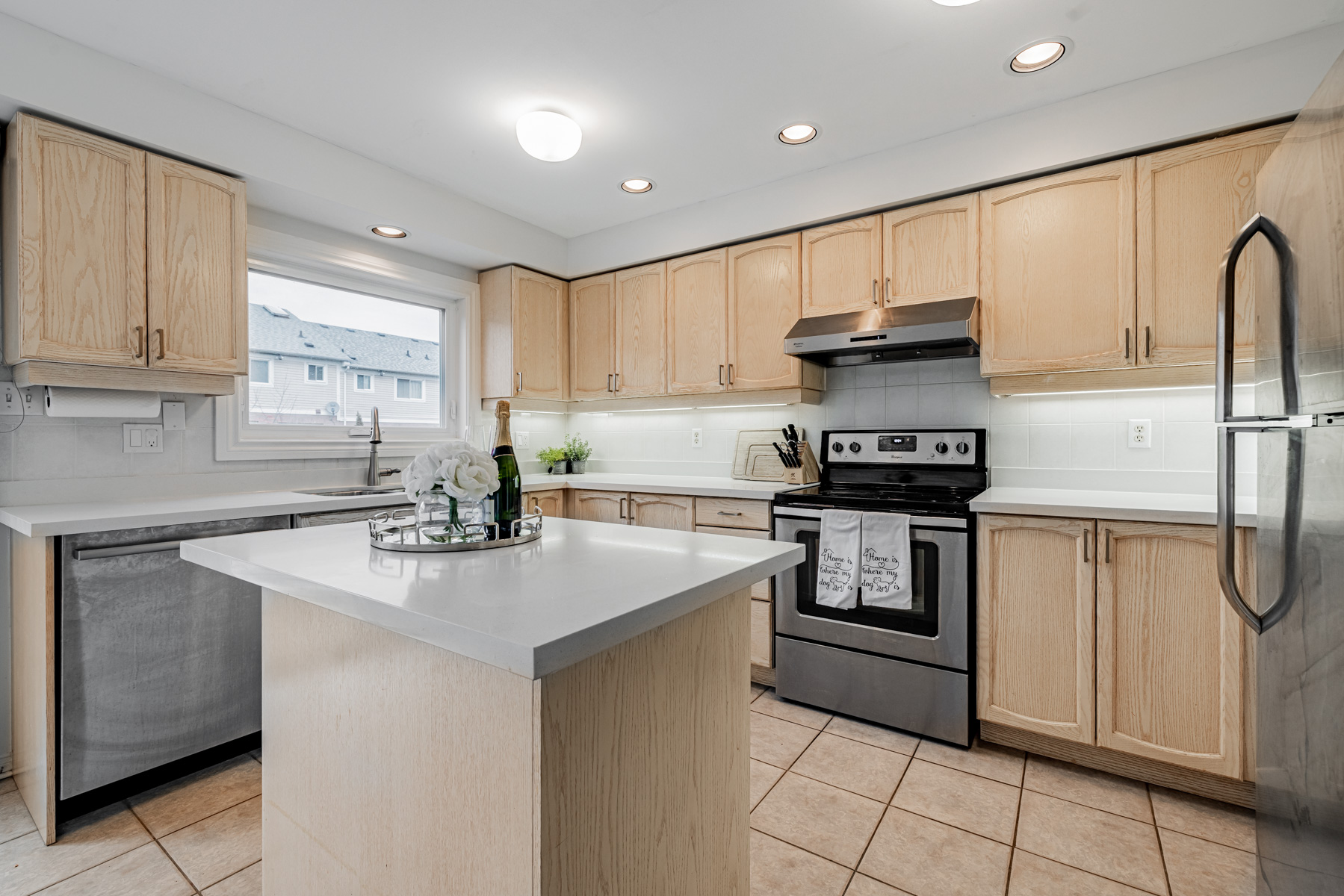 Kitchen lit by window, ceiling lamps and pot lights.