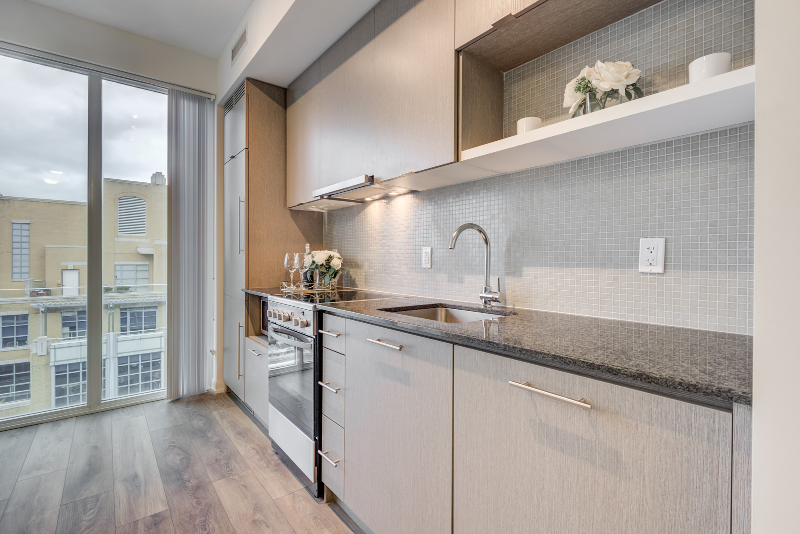 Close up of kitchen with black granite counters, chrome faucet, silver stove and grayish cabinets.