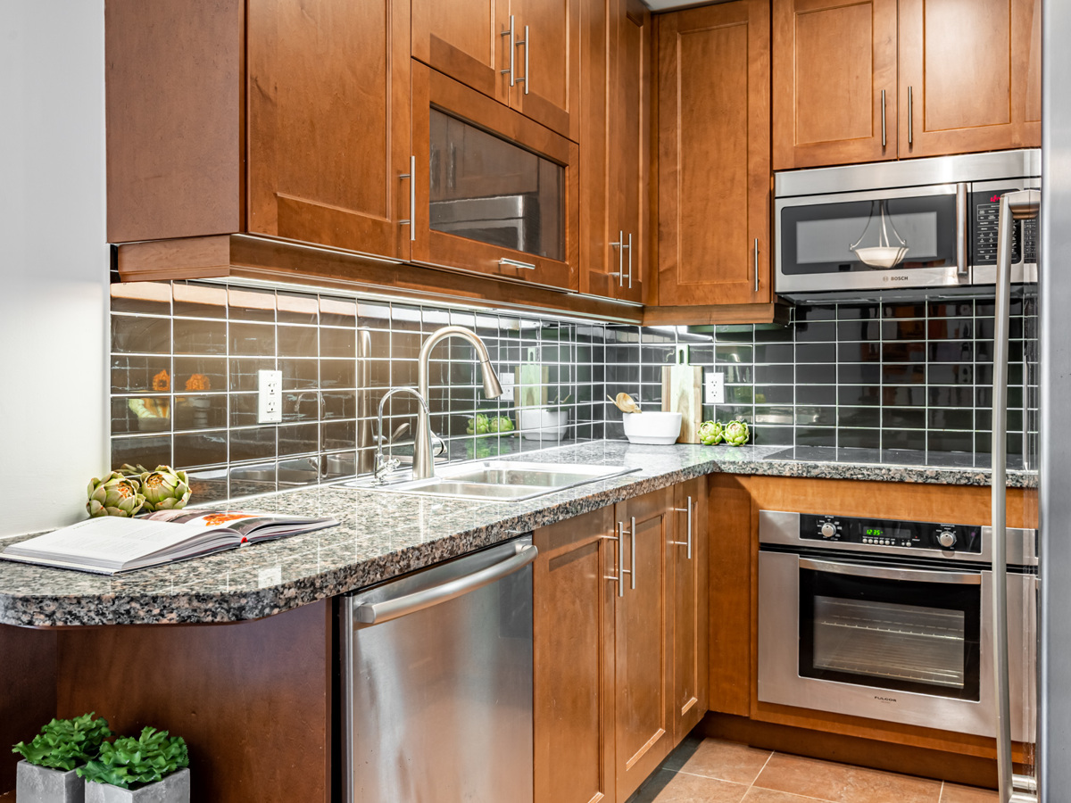 Beautiful condo kitchen with black granite counters, wood cabinets and black tiled back-splash.