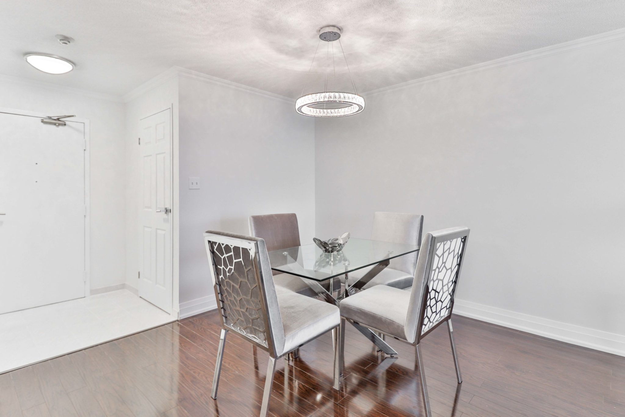 Dining room with glass table, 4 chairs and round chandelier.