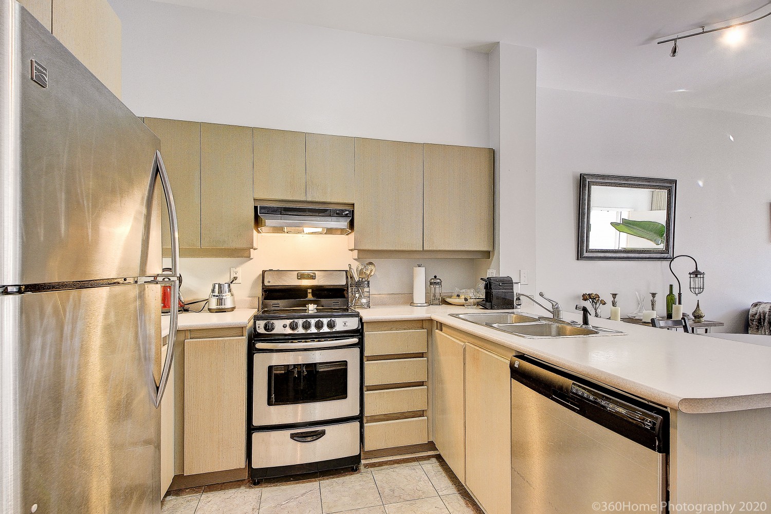 Somewhat old condo kitchen with beige cabinets, marble tiles and stainless-steel stove and fridge.