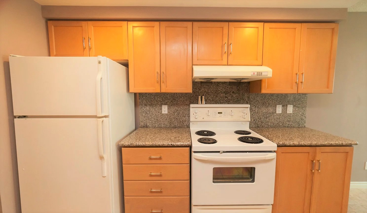 68 Simcoe kitchen with white fridge and stove, wooden cabinets and granite counters.
