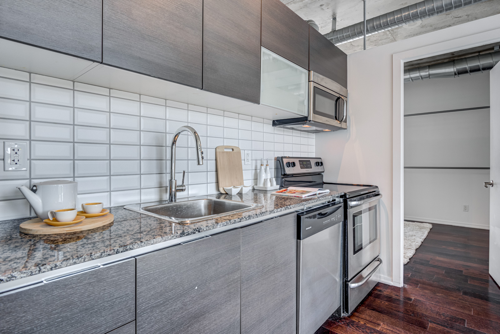 Kitchen back-splash with white tiles, dark cabinets and silver appliances.