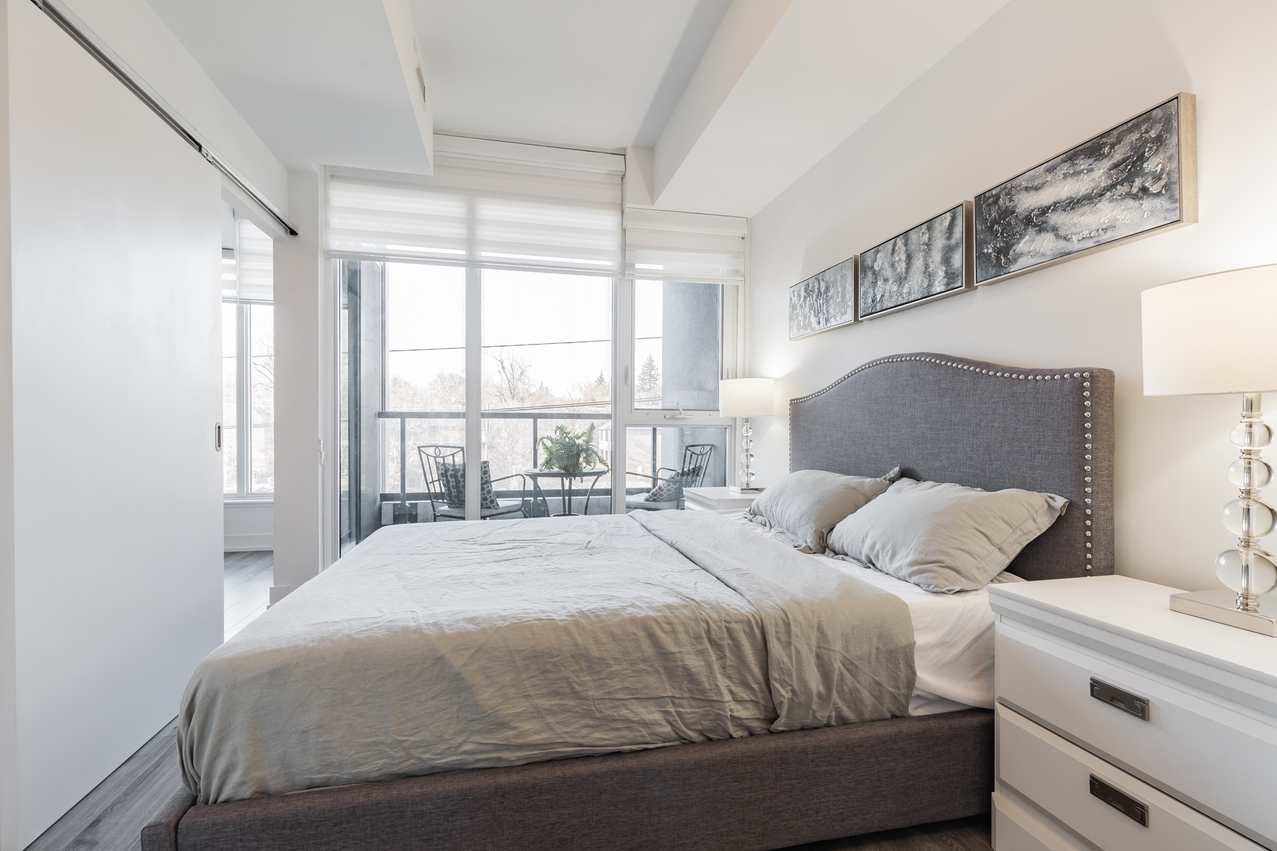 Brightly lit condo bedroom with bed overlooking balcony.