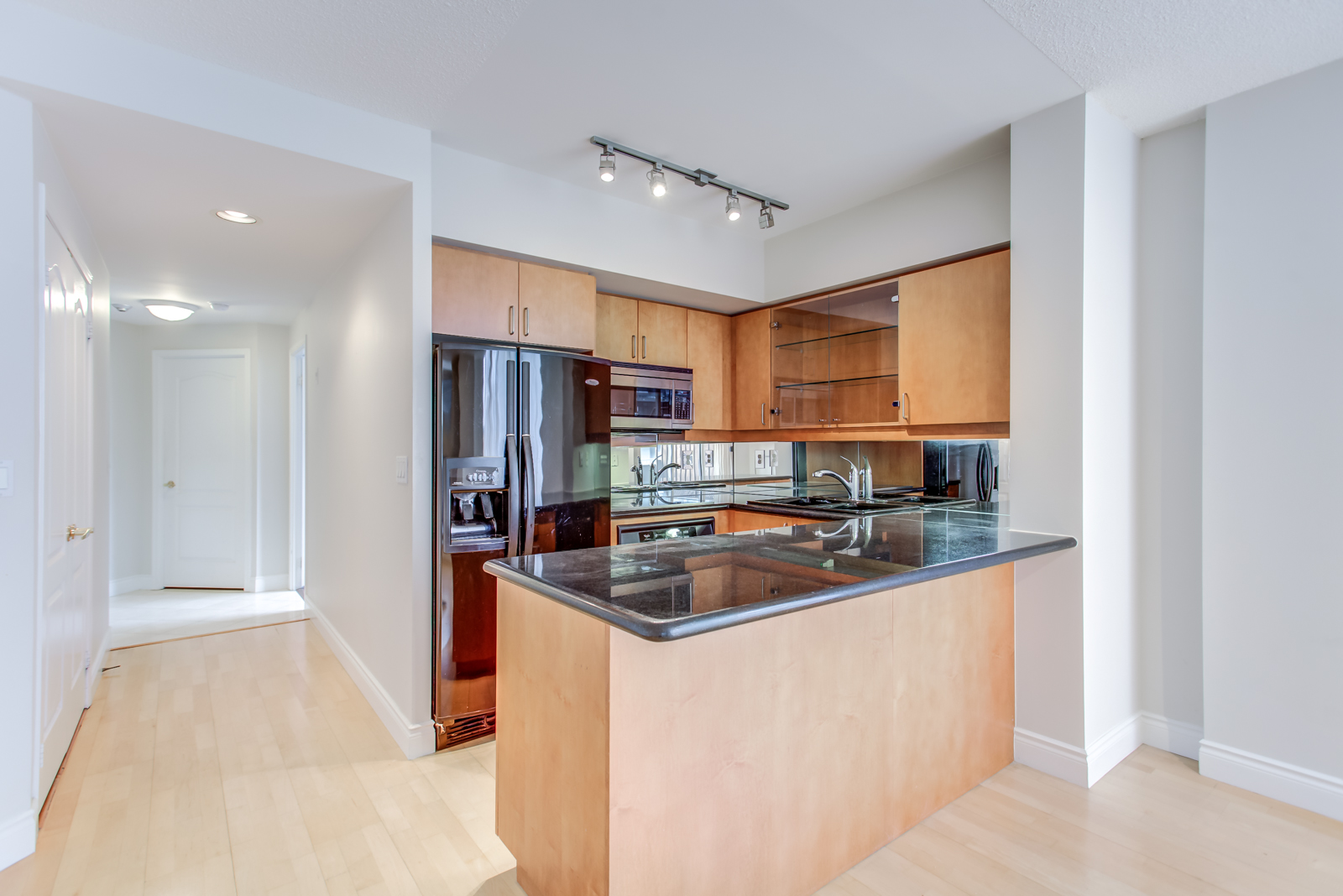 Kitchen with black counters, black fridge, wooden cabinets and track-lights.