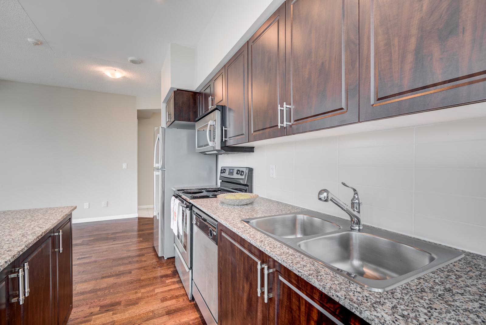 Close up of 215 Fort York Blvd kitchen with speckled granite counters and dark wood cabinets.