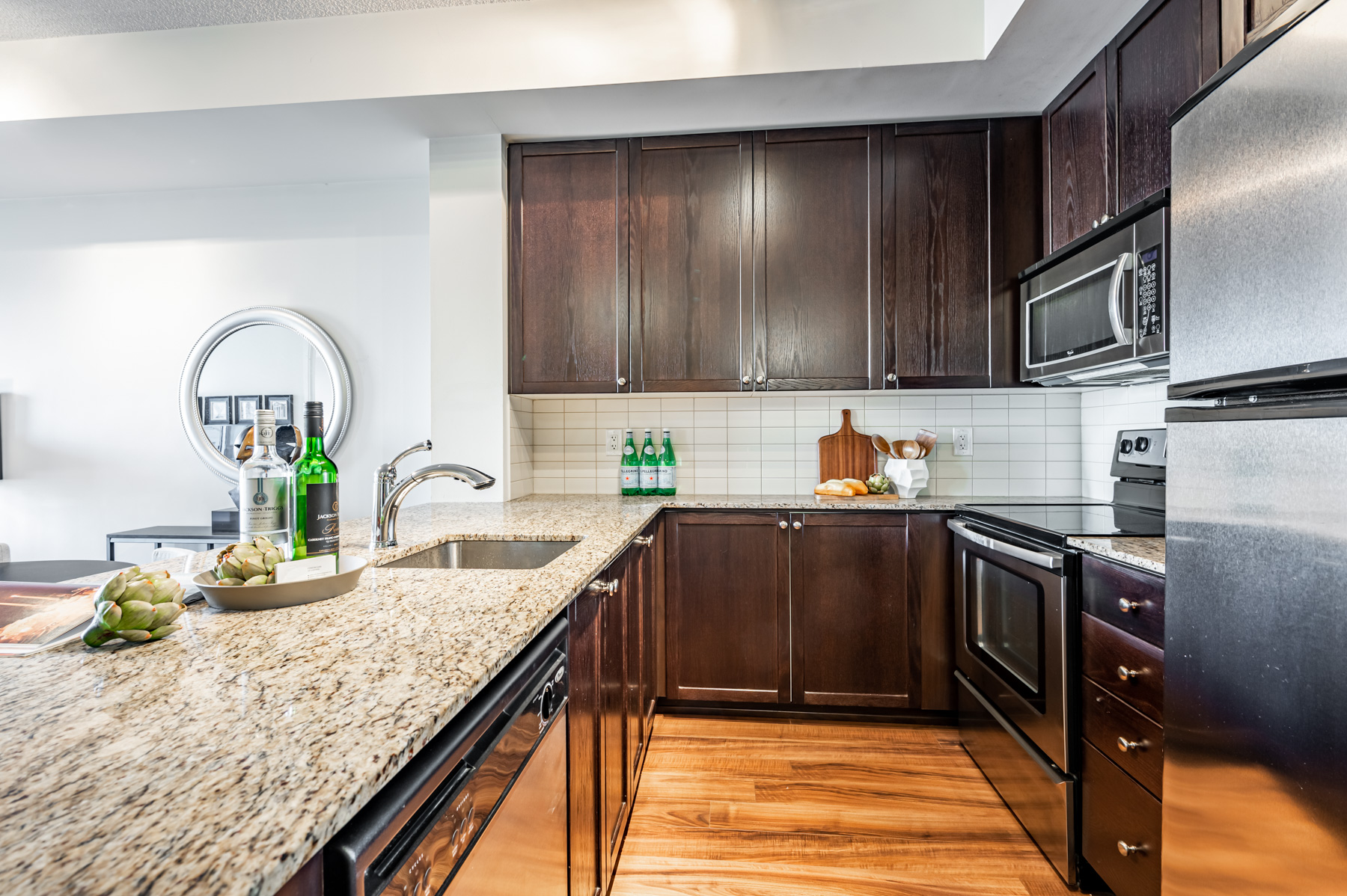 U-shaped condo kitchen with granite counters, dark wood cabinets and porcelain backsplash.
