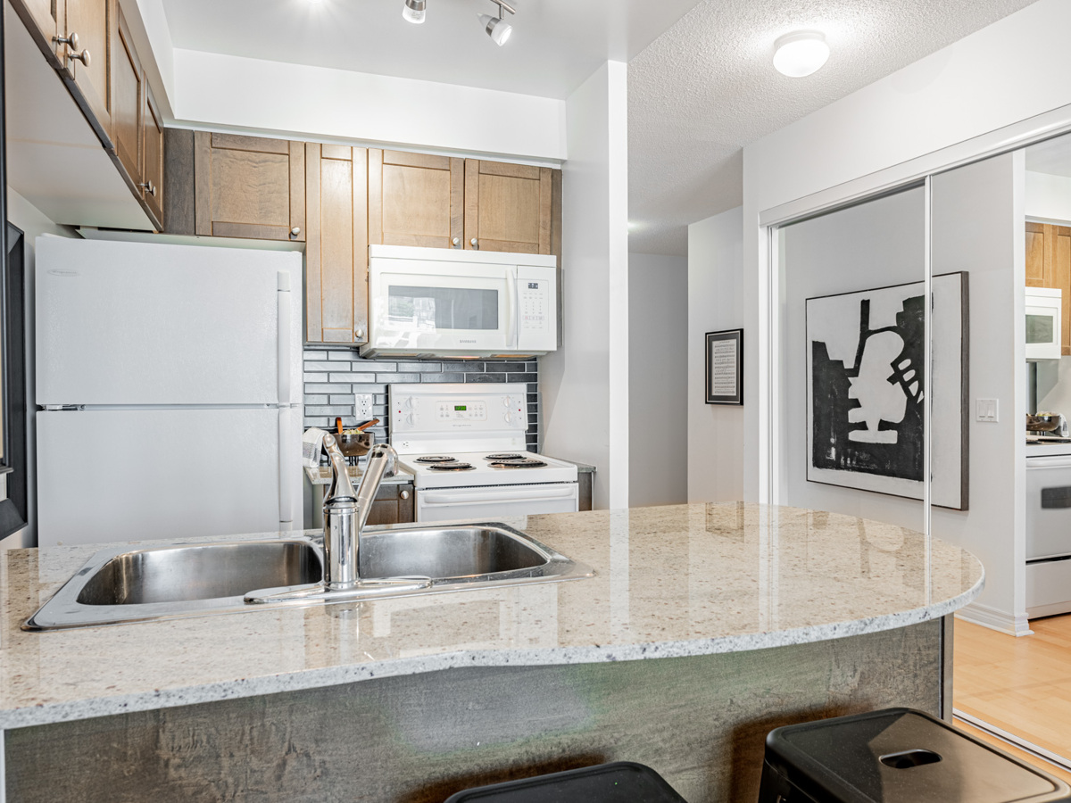 Cabinets, counters, back-splash and appliances shining under kitchen track-lights.