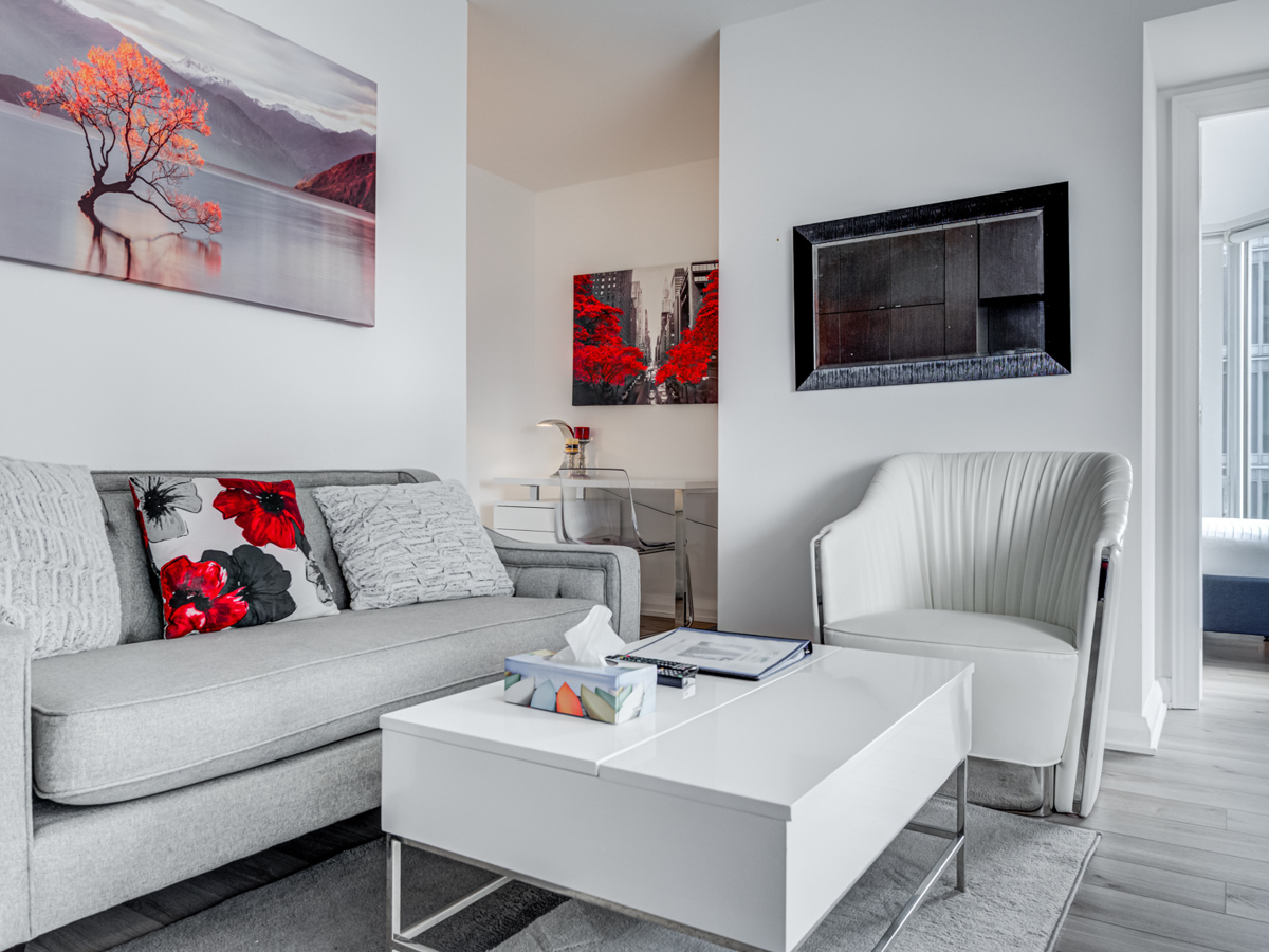 Living room with gray walls, floor and furniture with colourful paintings and pillow.