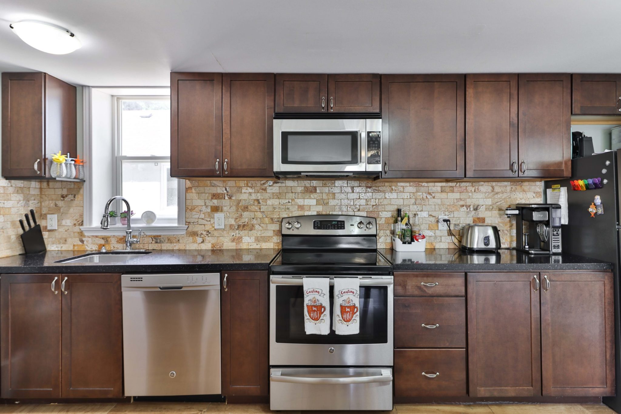 Kitchen with stainless-steel appliances, black granite counterd, dark cabinets and stylish brick back-splash.