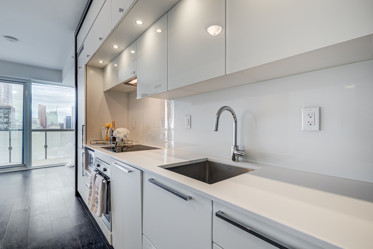 White kitchen cabinets, counters, backsplash and pot-lights.