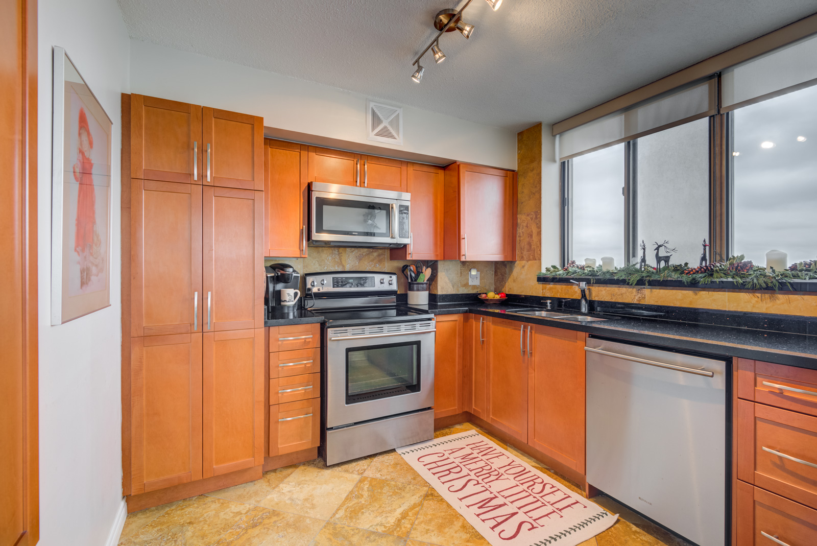 Large kitchen with orange oak cabinets, drawers, silver appliances, slate floors and track-lights.