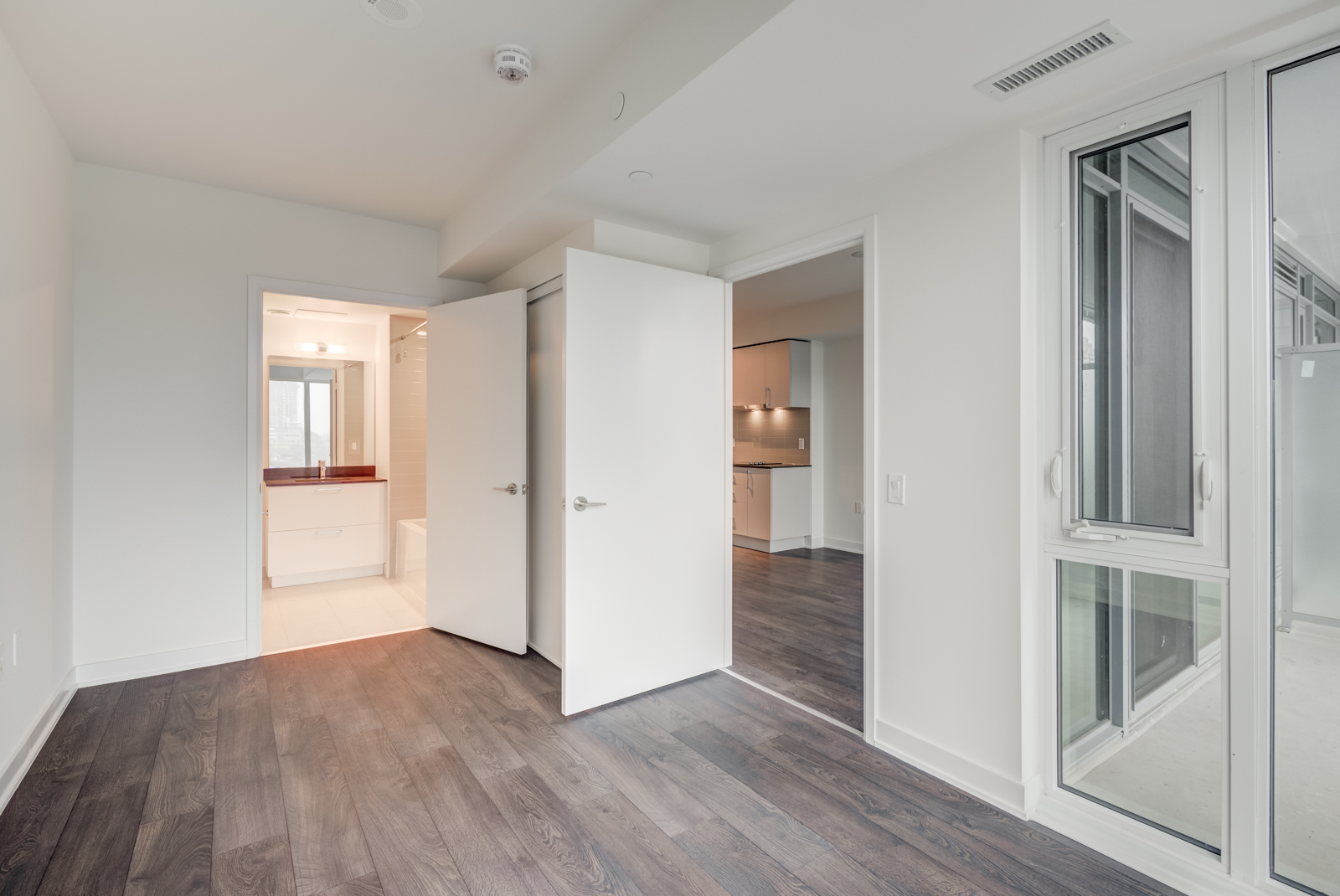 Empty master bedroom with dark laminate floors and gray walls.