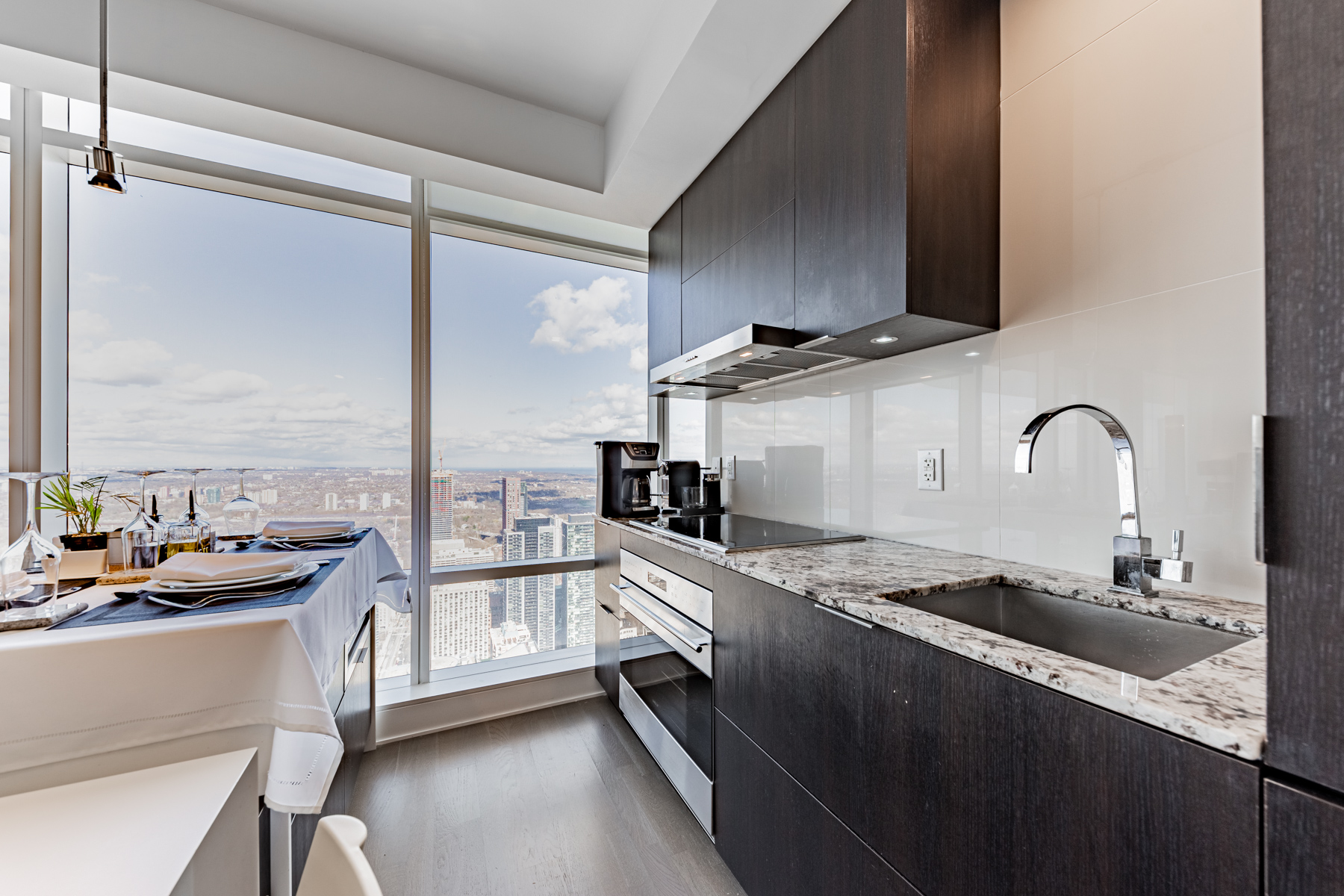 Condo kitchen with dark wood cabinets, marble counters, tiled back-splash & pot-lights.