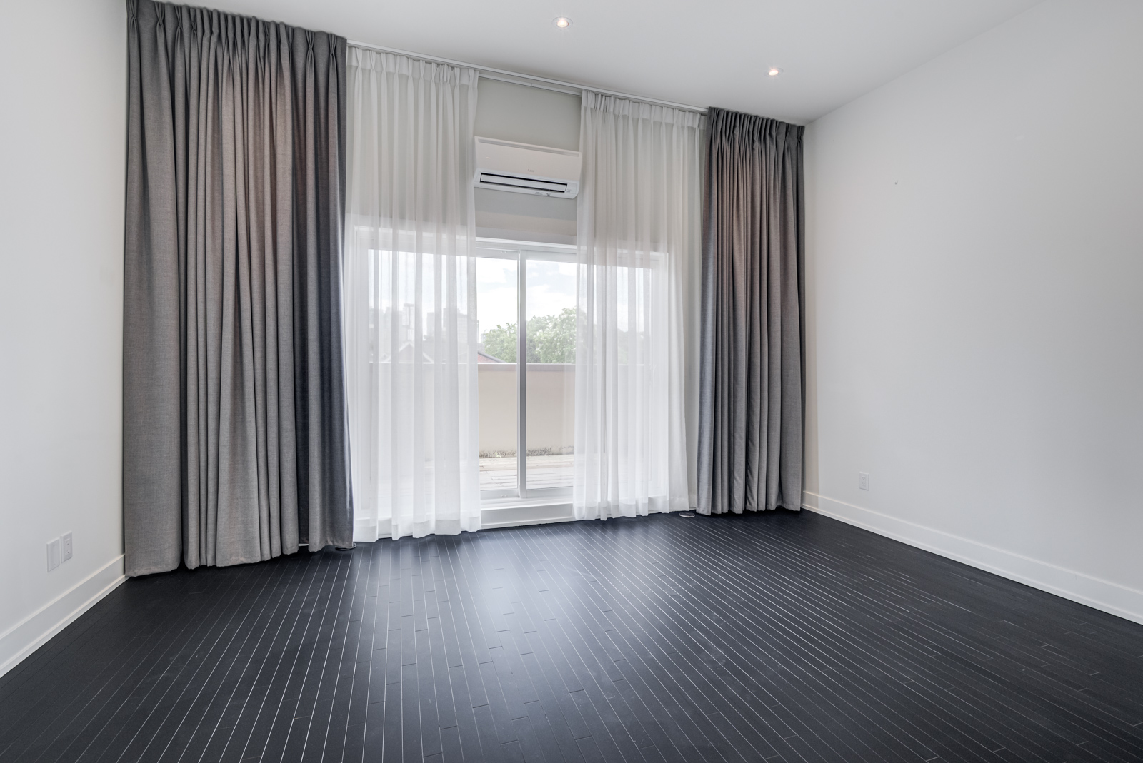 Empty master bedroom with black floors and white and gray curtains