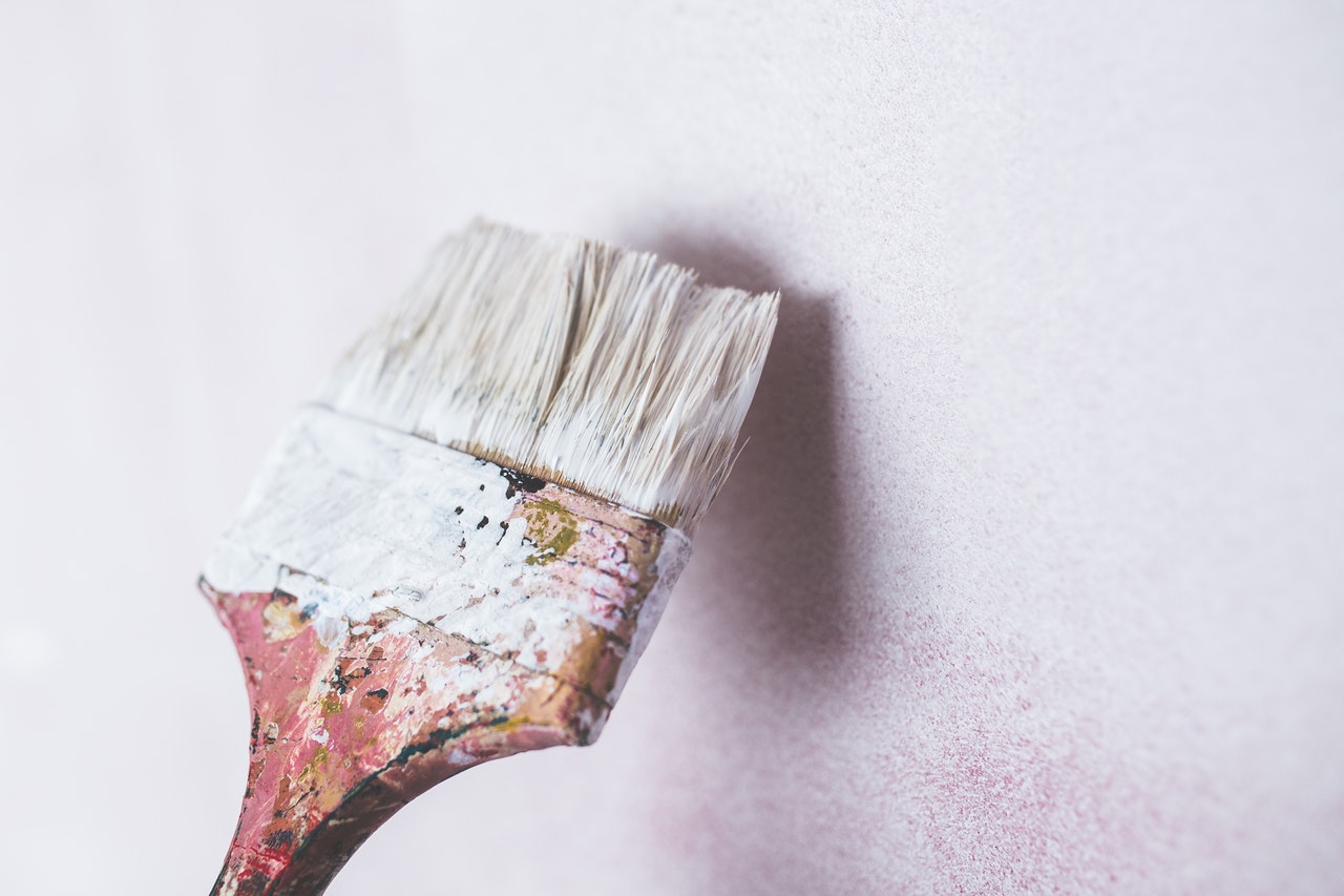 Image of a paint brush covered in white paint and a wall.