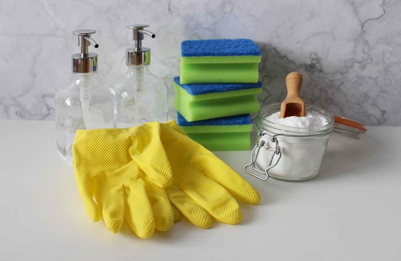 Close up of yellow gloves, sponges and cleaning supplies.