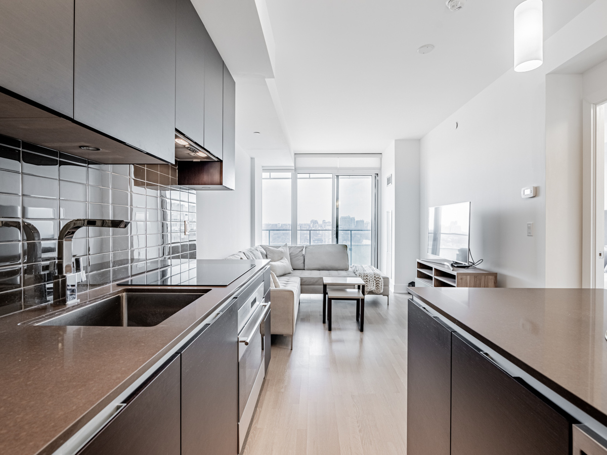 Condo kitchen with under-cabinet lights, dark quartz counters and porcelain back-splash.