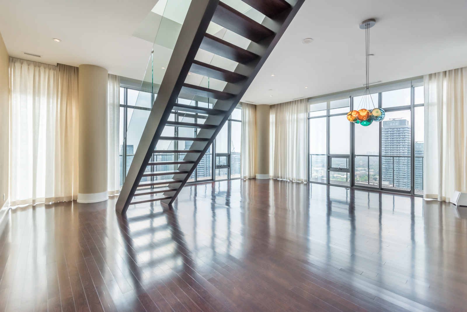Empty penthouse with shiny floors and staircase with glass panels; most expensive property at 33 Charles St E Casa Condos.