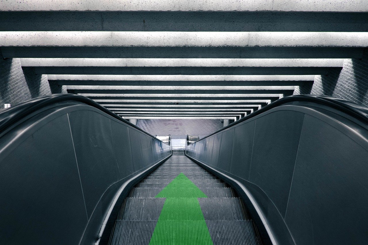 Escalator with downward arrow symbolizing need to buy home now.