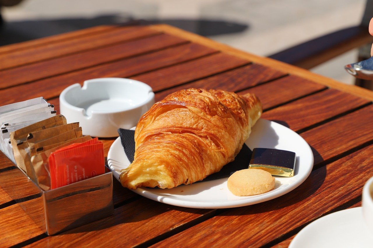 French cafe with large wood table and croissant on white plate.