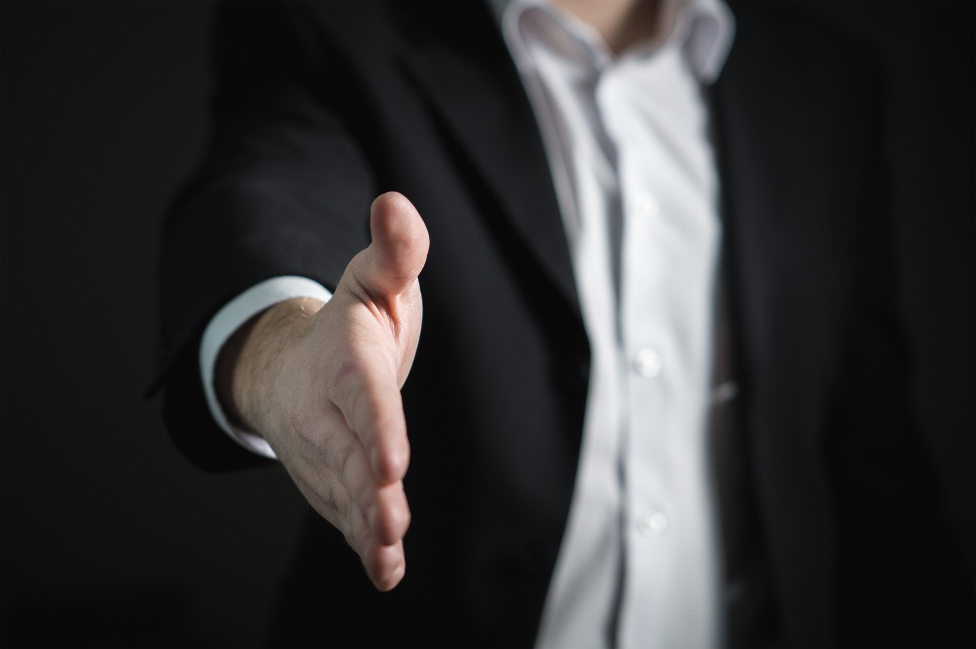 Man reaching out to shake hand. He is wearing a suit to show how hiring a realtor needs to dress the part. 