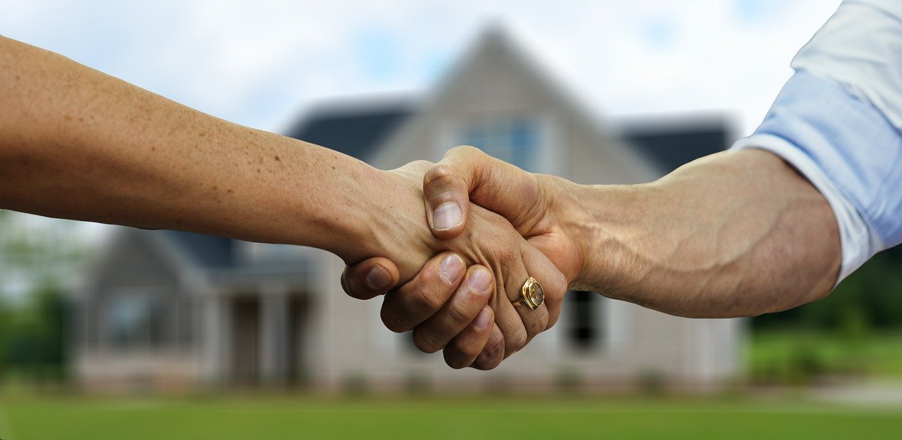 Handshake in foreground; house in background.