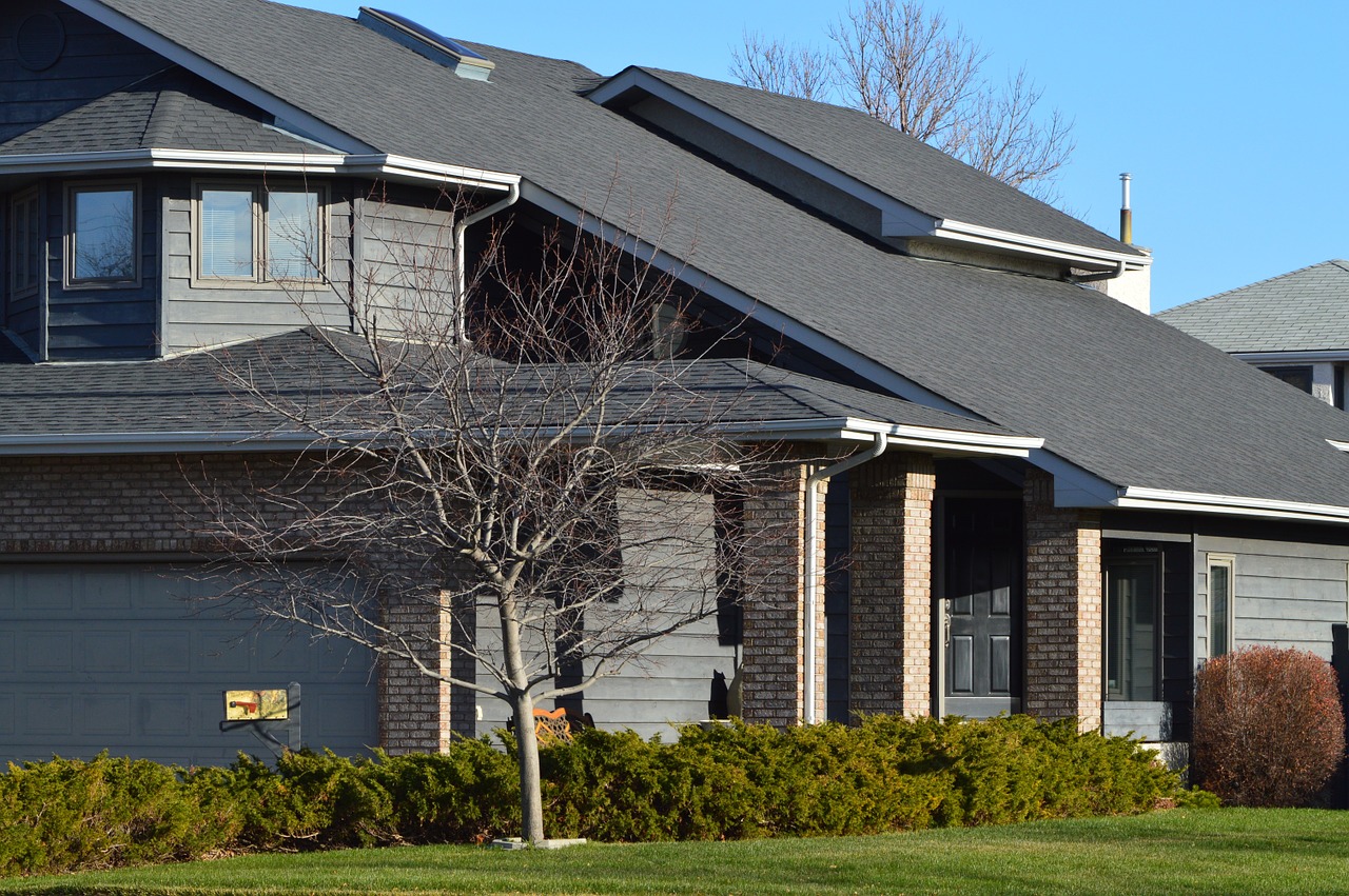 House in suburbs; we see a tree and bushes and lawn and MLS.