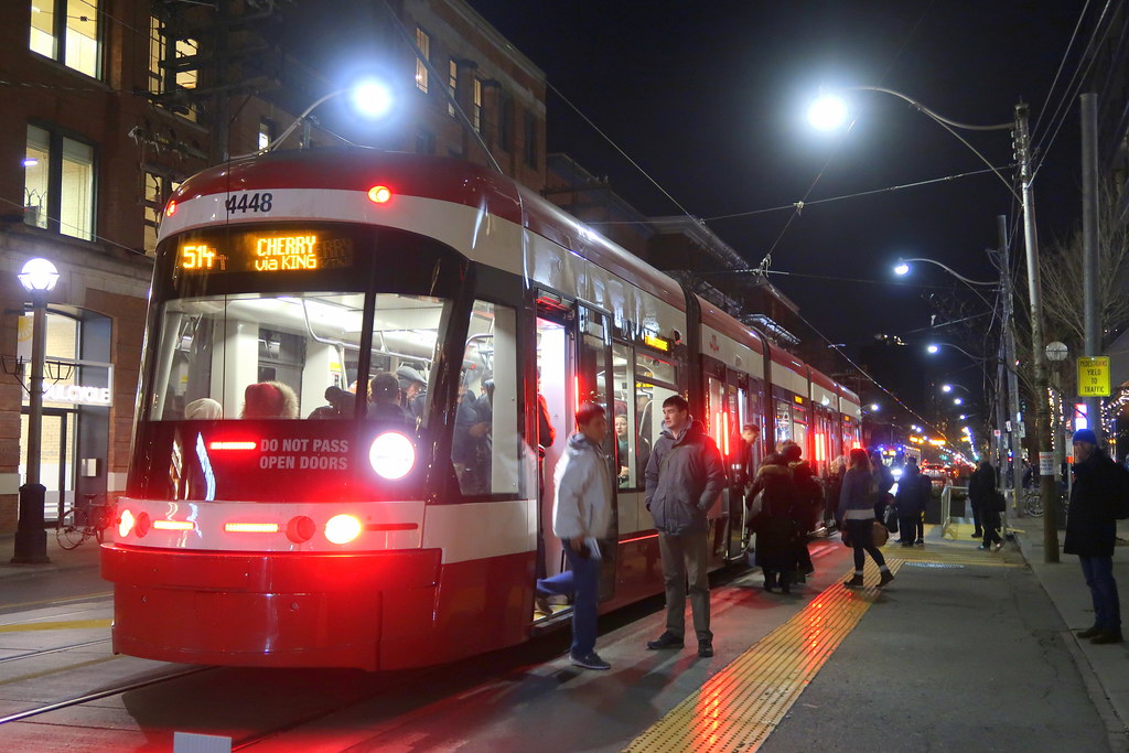 People getting on red streetcar on King St W, Toronto.