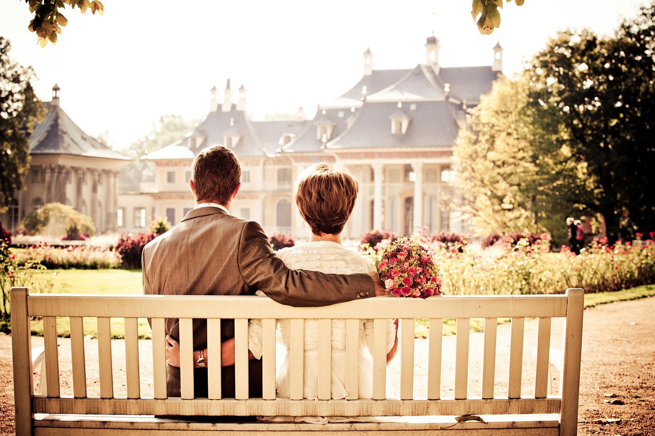 Married couple sitting on bench looking at house.