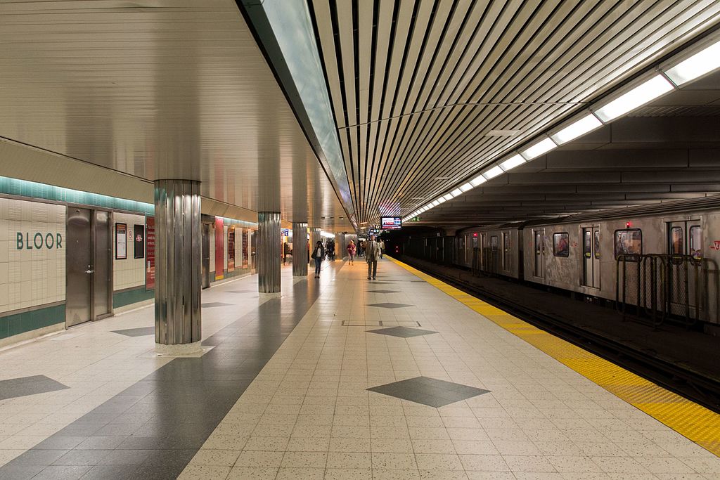 Brightly subway platform with people and train old TTC train to right in Toronto.