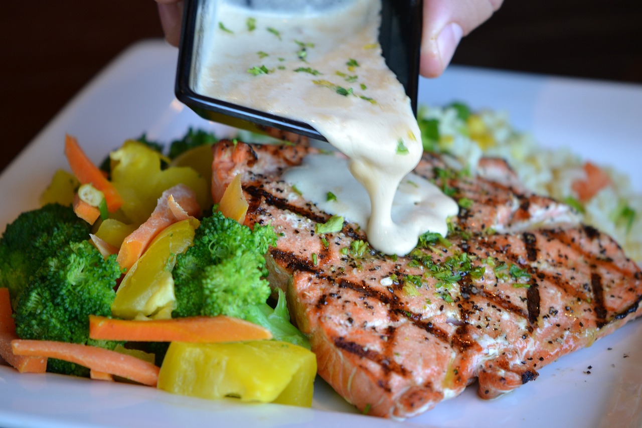 Plate of salmon with white dip being poured on top. 