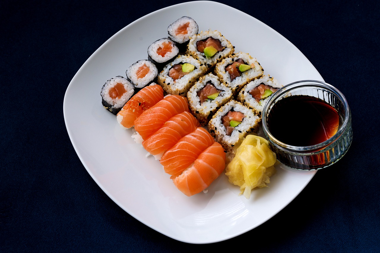 Sushi on white plate with soy sauce in glass bowl.