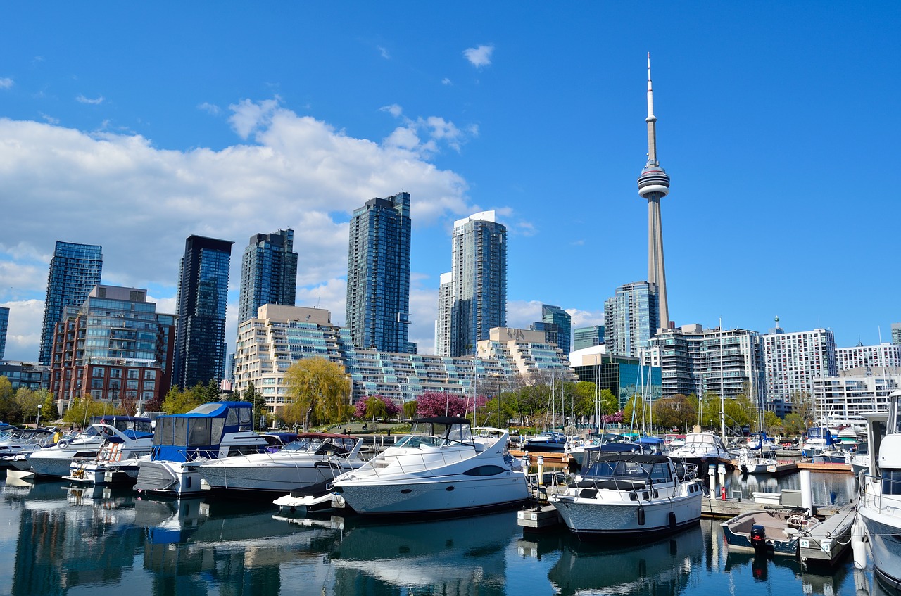 Boats at Toronto pier with CN Tower and luxury real estate in background.