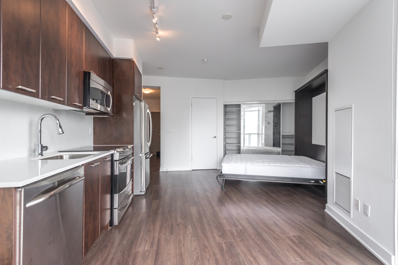 Image of condo showing kitchen, open bed, and also the brown floors.