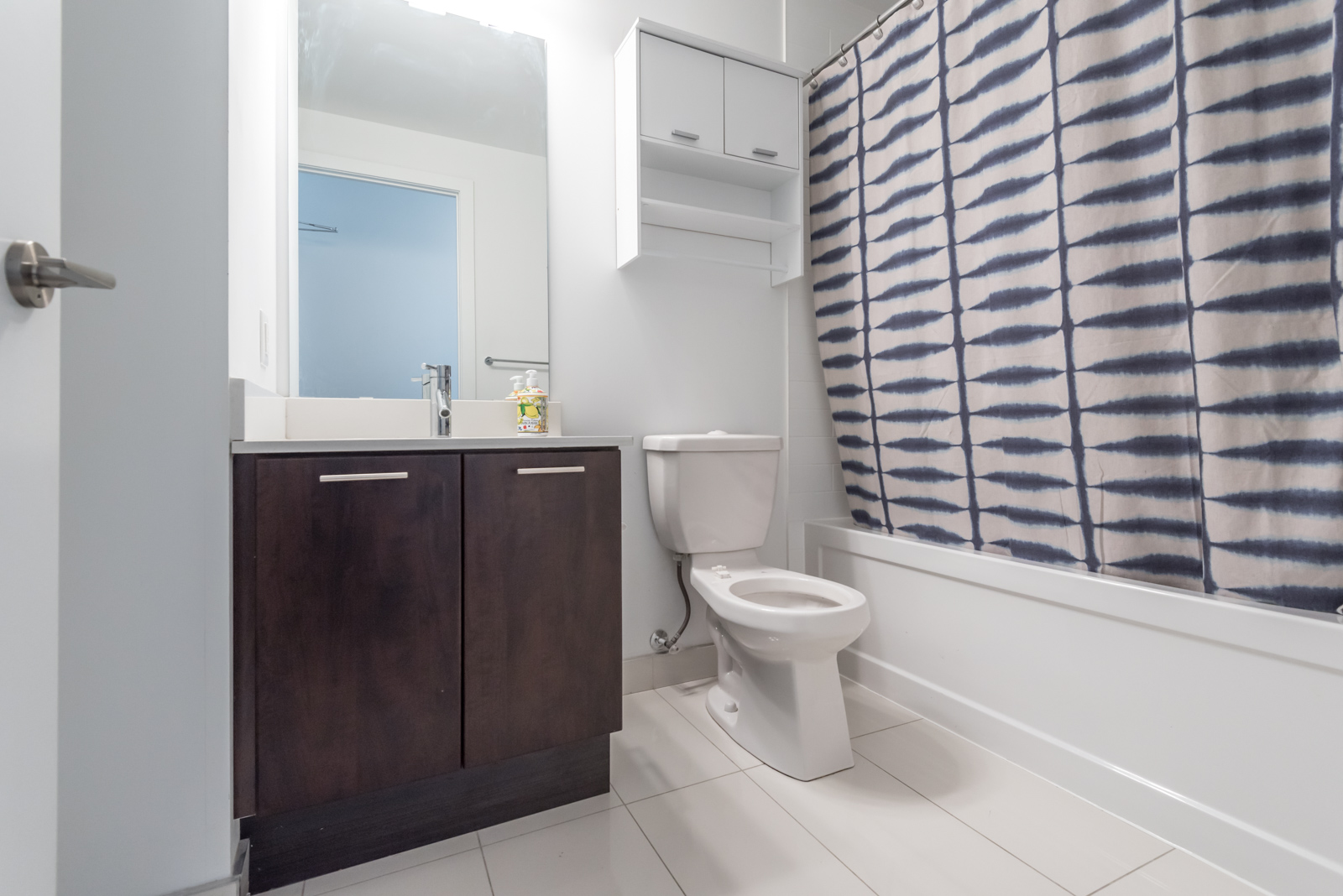 Bathroom with white and brown colours. We can also see the curtain, a rather large mirror, and finally, the tiles.