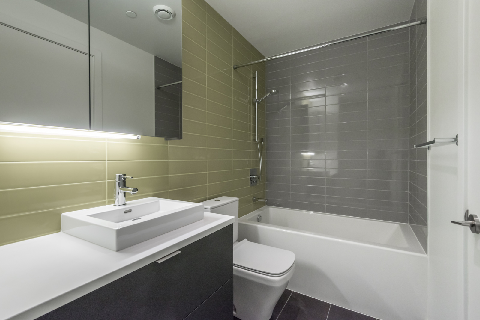 Image showing bathroom and tub. Also shows green and gray tiles, sink, and toilet.