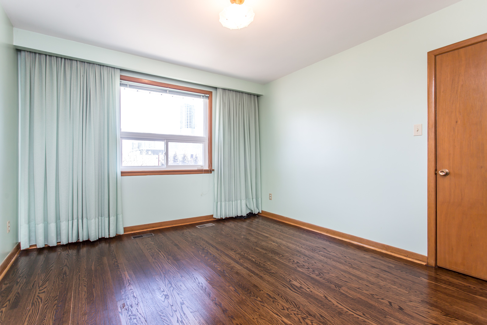 Image of master bedroom. The floors are rather dark, while the walls and curtains are less so.