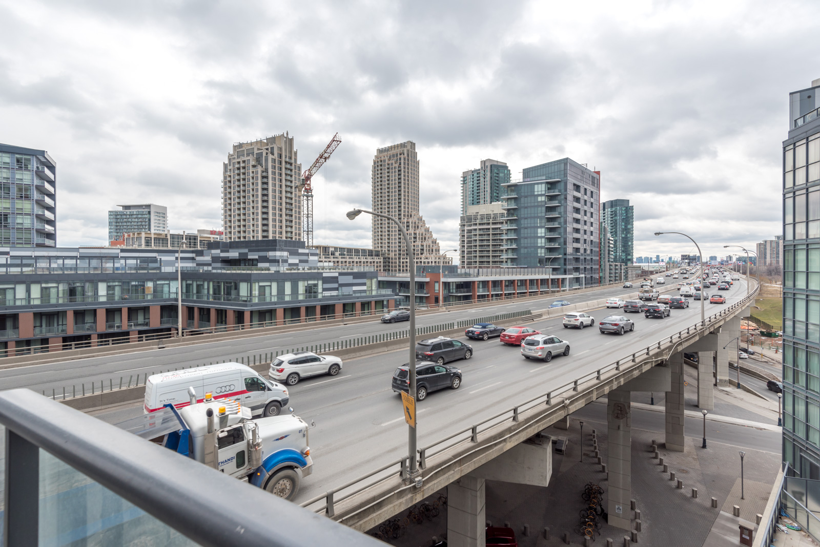 Balcony view from 169 Fort York Unit 710. We can see the highway with so many cars, and buildings in the background. There's also construction going on. Furthermore, the skies are gray and cloudy.