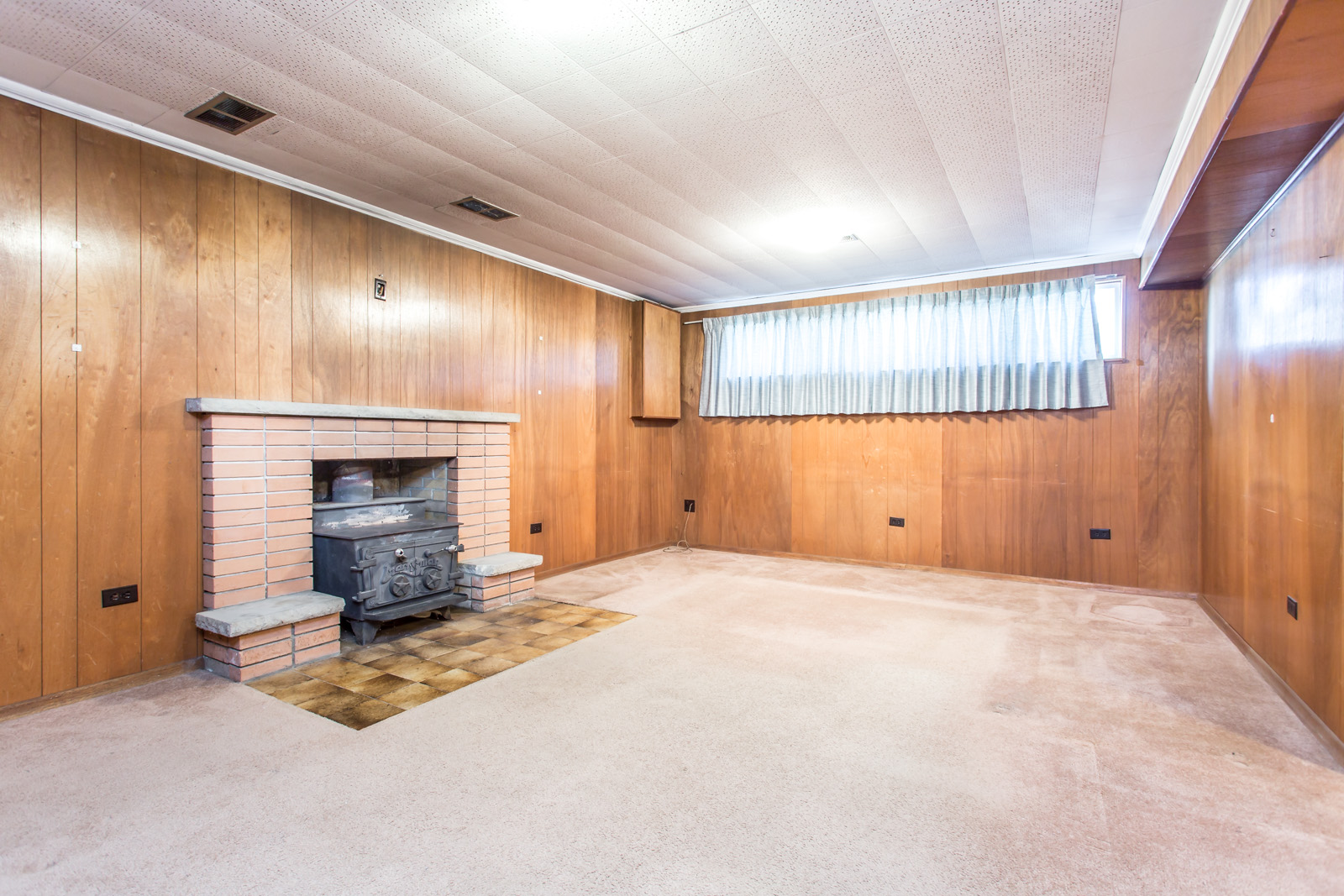 Rec room with carpet and furnace. Almost all of it is covered in carpet, while the walls have wooden panels.