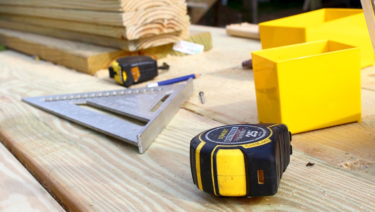 Close up of table with tape measure, triangle, wood pile, showing Phyxter contracting job.