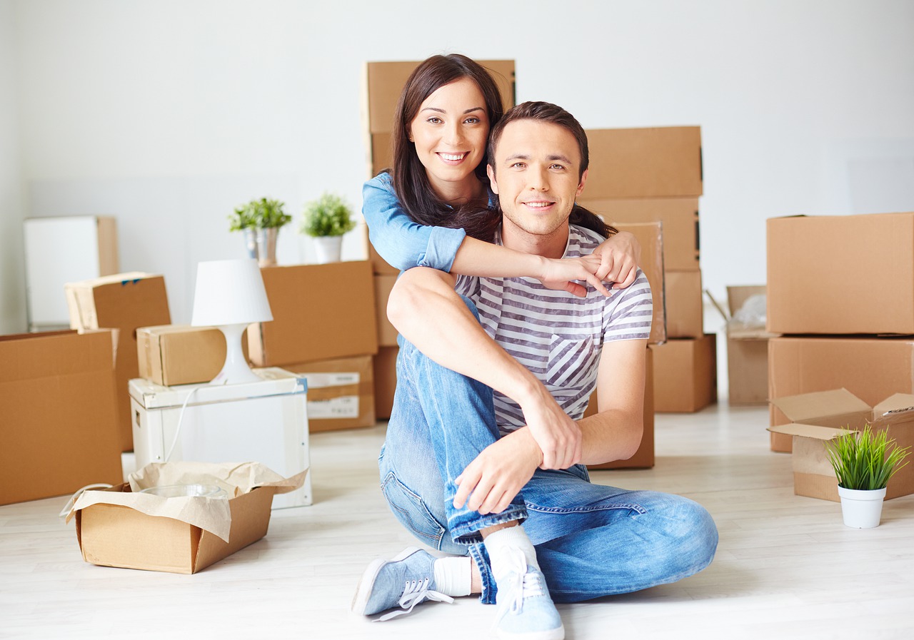Young couple sitting on floor embracing with moving boxes in background.