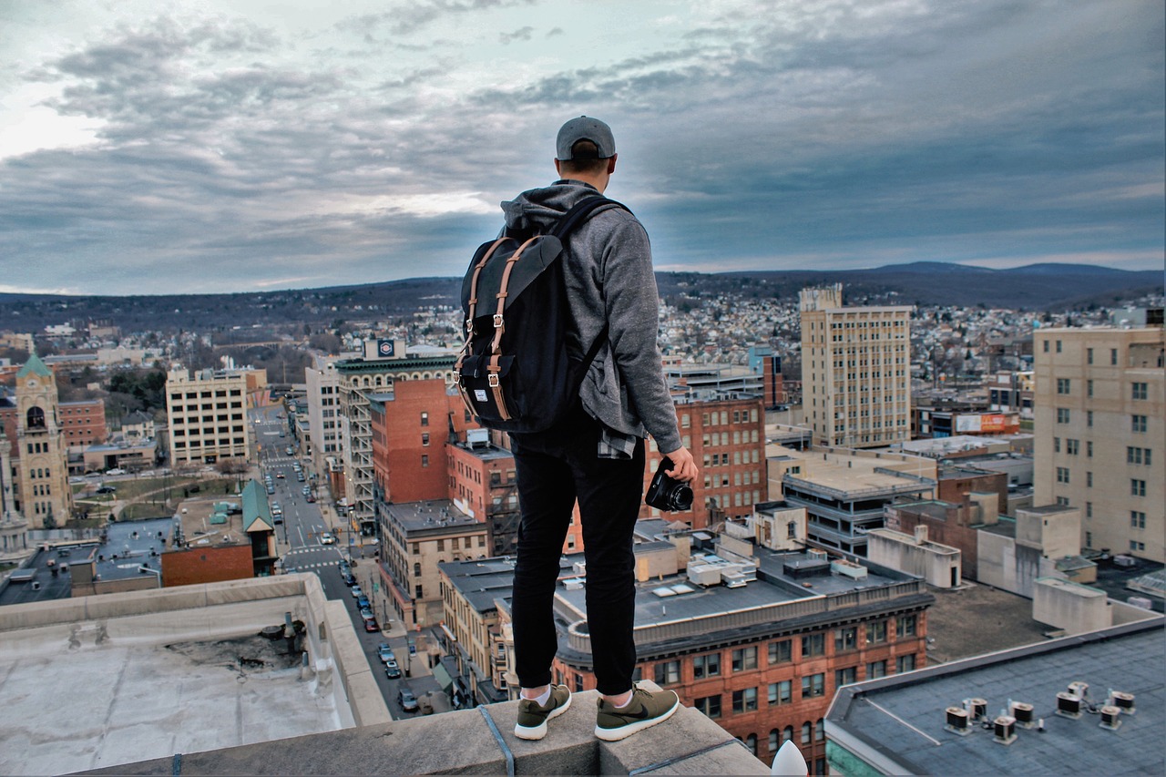 Young man standing on edge of building looking down at city.