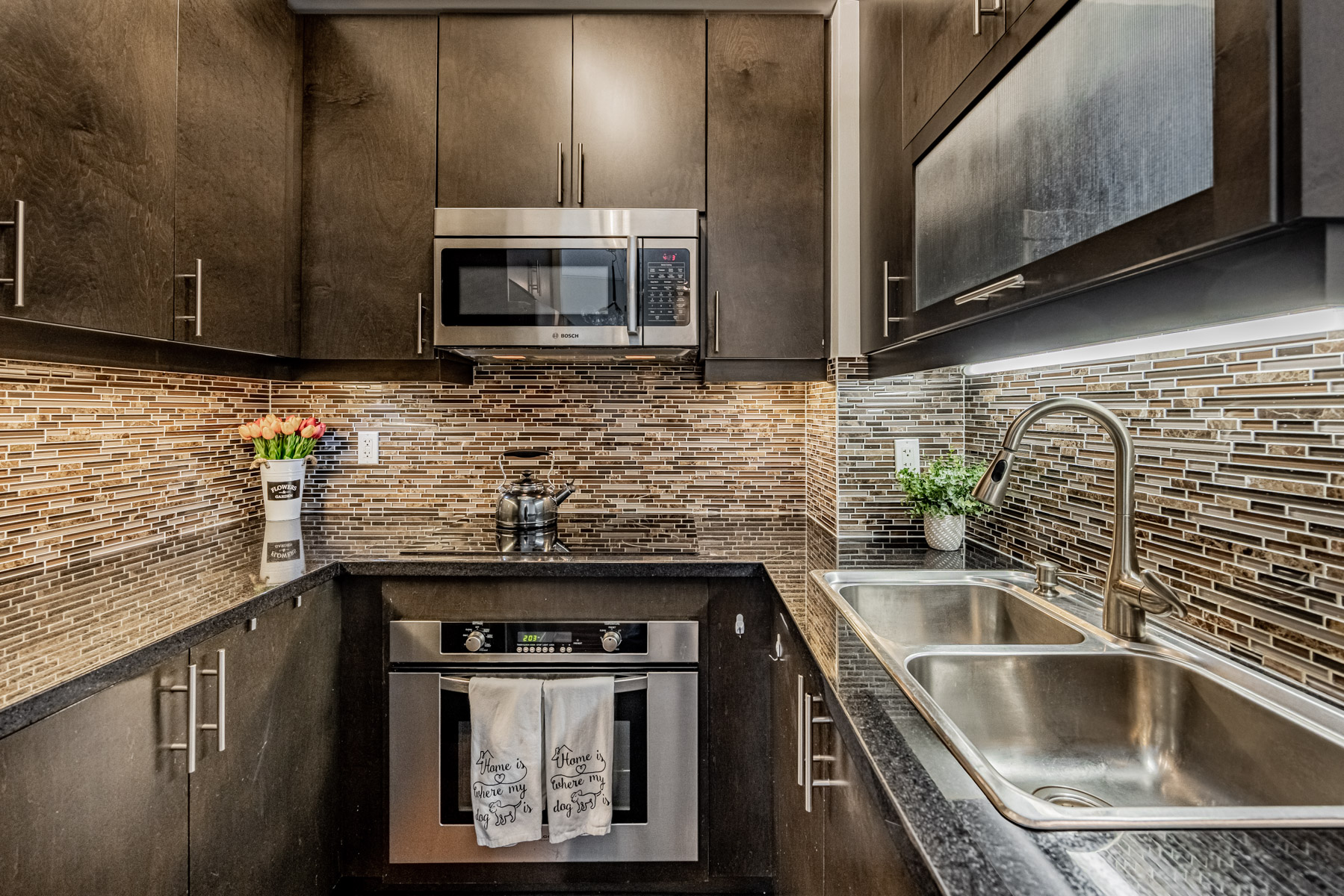 Dark condo kitchen with black granite counters, hardwood floors and dark ceramic back-splash.