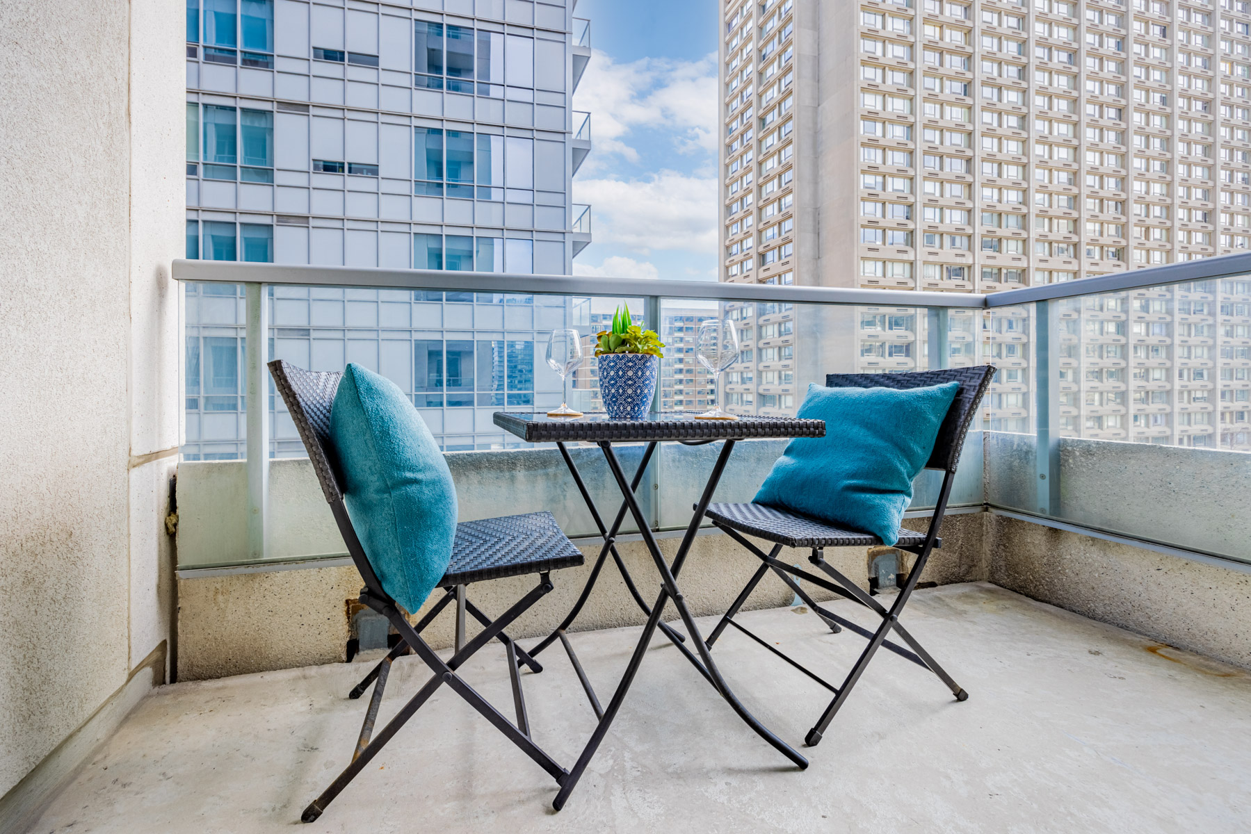 Condo balcony with 2 chairs and table with wine glasses.