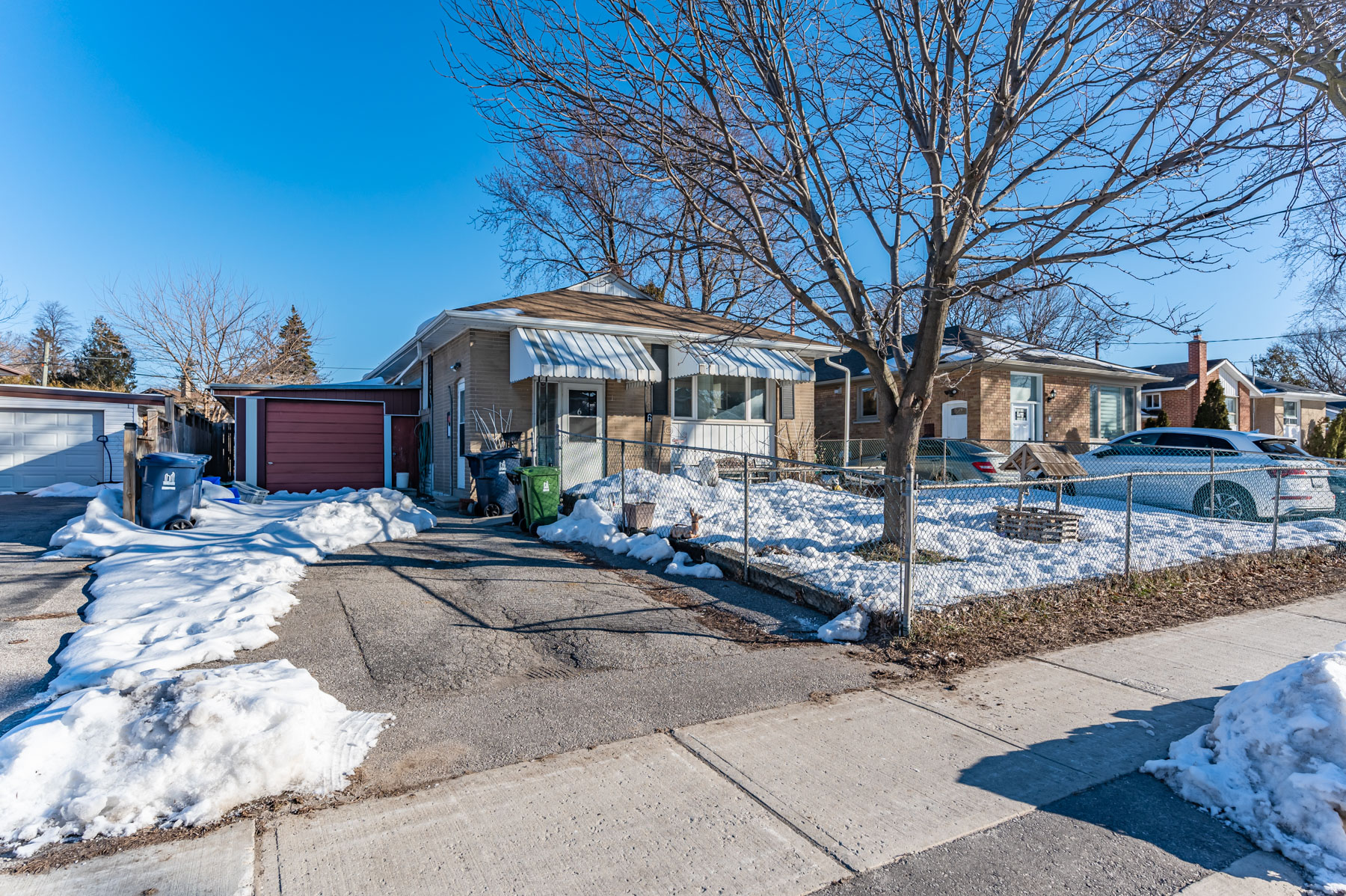 Bungalow with snow-covered driveway and red-door garage.