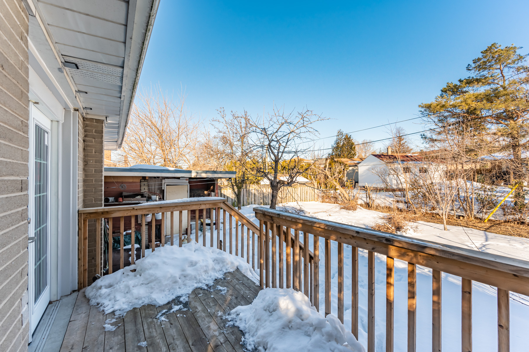 Backyard deck covered in snow and with view of trees.