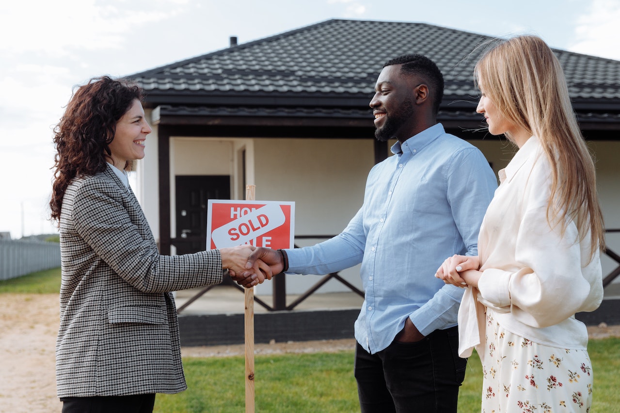 Two people shake hands outside house with sold sign. 